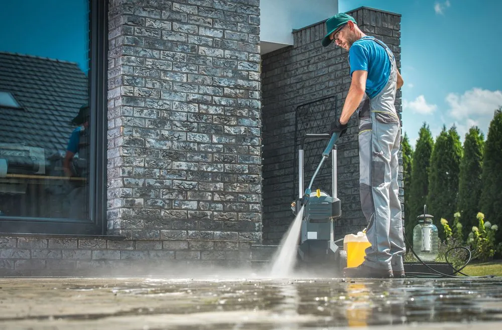 Man power washing brick wall and concrete patio.